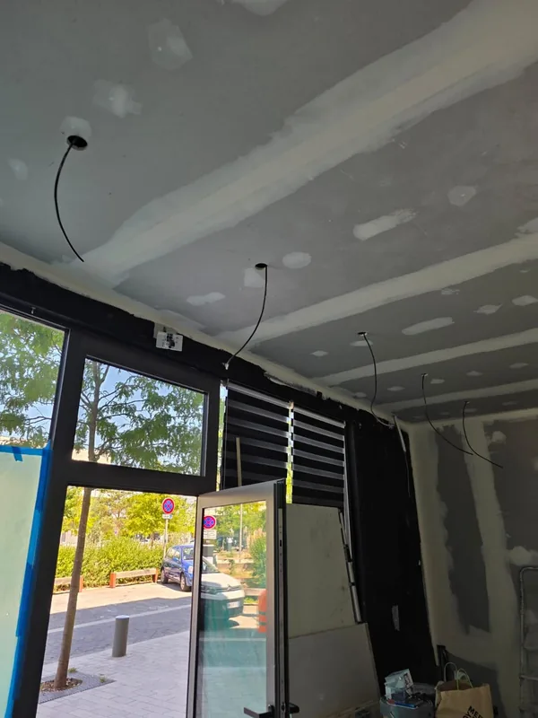 Câblage électrique au plafond d'un local avec baie vitrée sur rue, cloisons en cours de finition